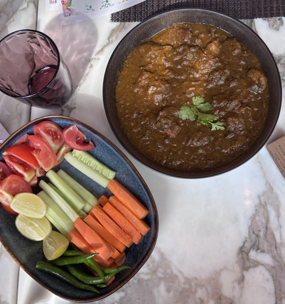 Authentic Hyderabadi beef curry in a black bowl with fresh vegetables and lemon slices.