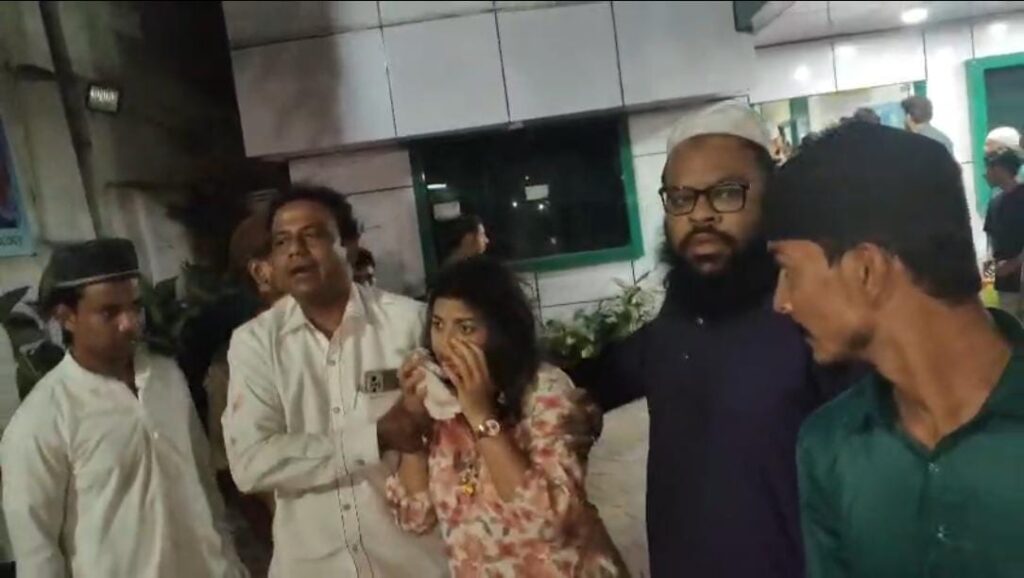 A group of people, including a woman drinking water, gathered outside a building at night.