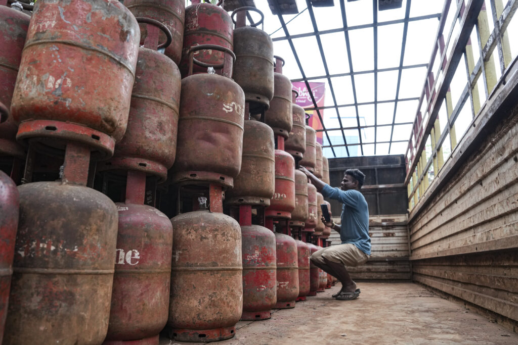 LPG cylinders stacked in a warehouse, with a man inspecting them, highlighting supply issues affecting Hy.