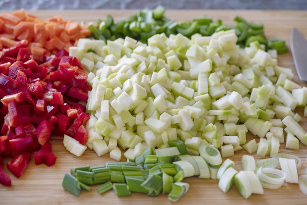 Chopped vegetables including red bell peppers, white onions, and green spring onions, prepared for a meal.