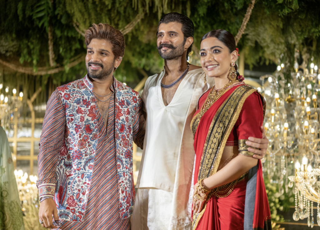 Three people in traditional Indian attire at a festive outdoor event, surrounded by greenery and decorati.