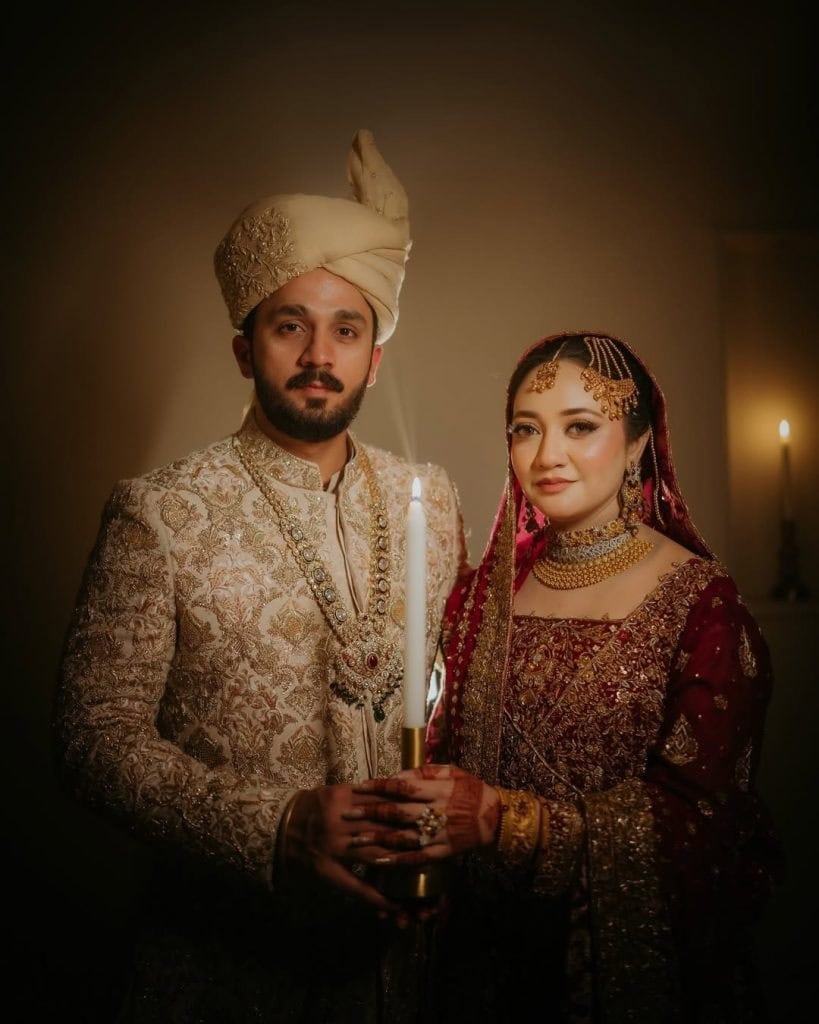 Wedding couple in traditional Pakistani attire, holding a candle during a cultural ceremony.