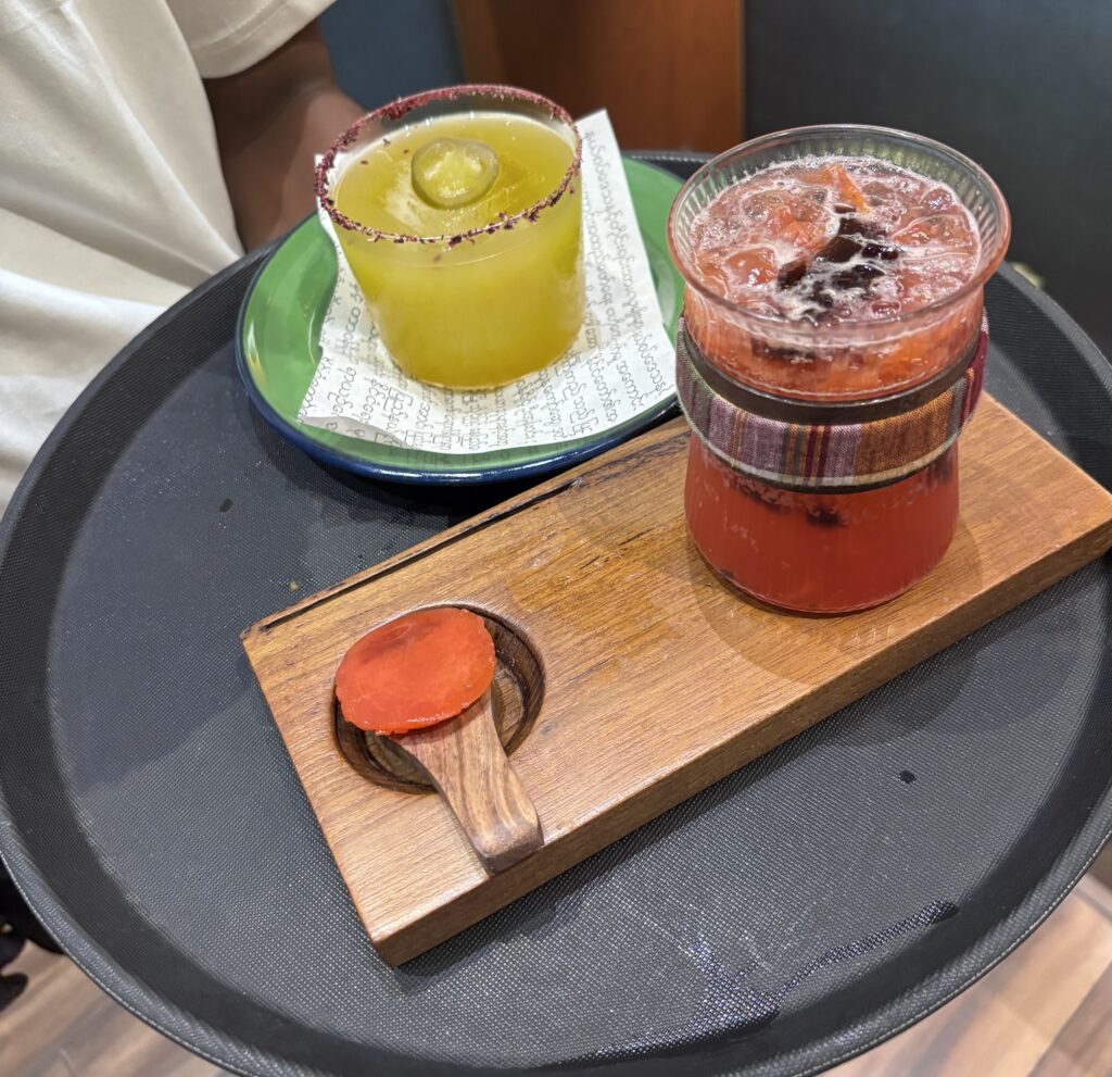 Vibrant cocktails served on a wooden tray at Burma Burma, featuring colourful drinks with garnishes, perf.