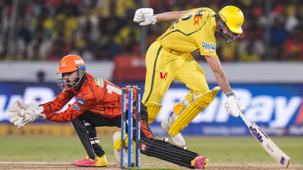 Cricket player in yellow uniform reaching for the ball while a wicketkeeper in orange dives to stop it.