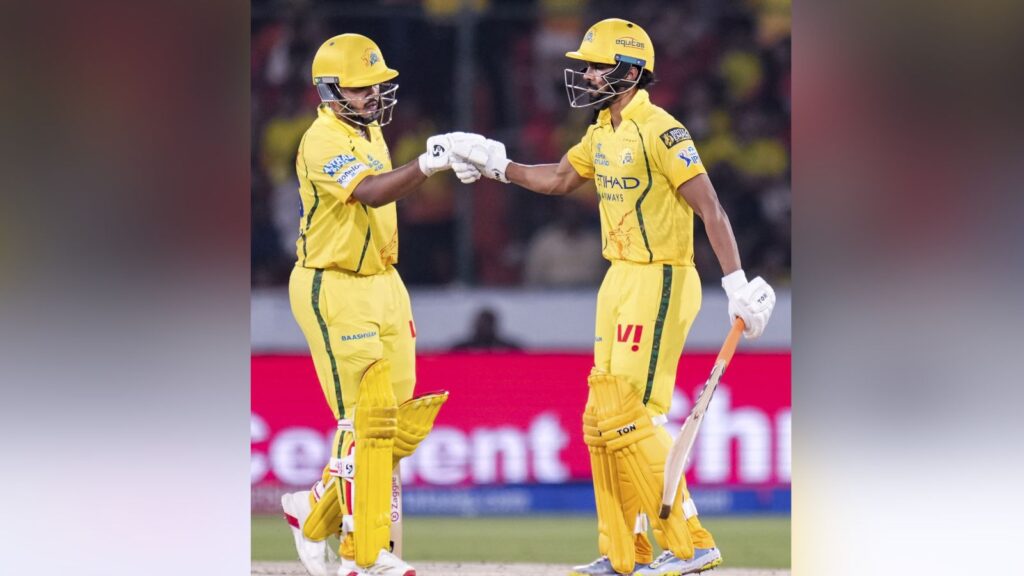 An image of two cricket players in yellow uniforms exchanging a fist bump on the field during a match.