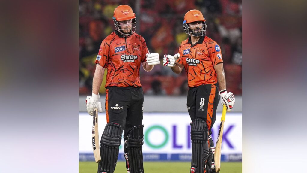 Two Delhi Capitals cricketers in orange jerseys celebrating on the field.