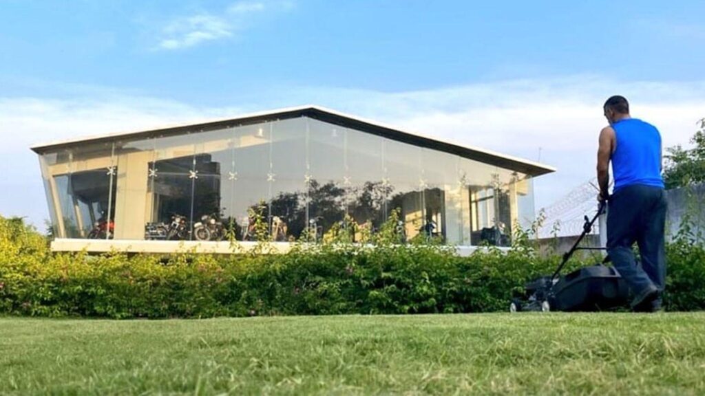Contemporary glass structure with a person trimming the grass in a lush green area.