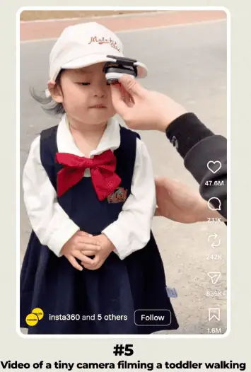 Child wearing a pink cap and navy dress, being filmed with a small camera on her forehead during a walk.