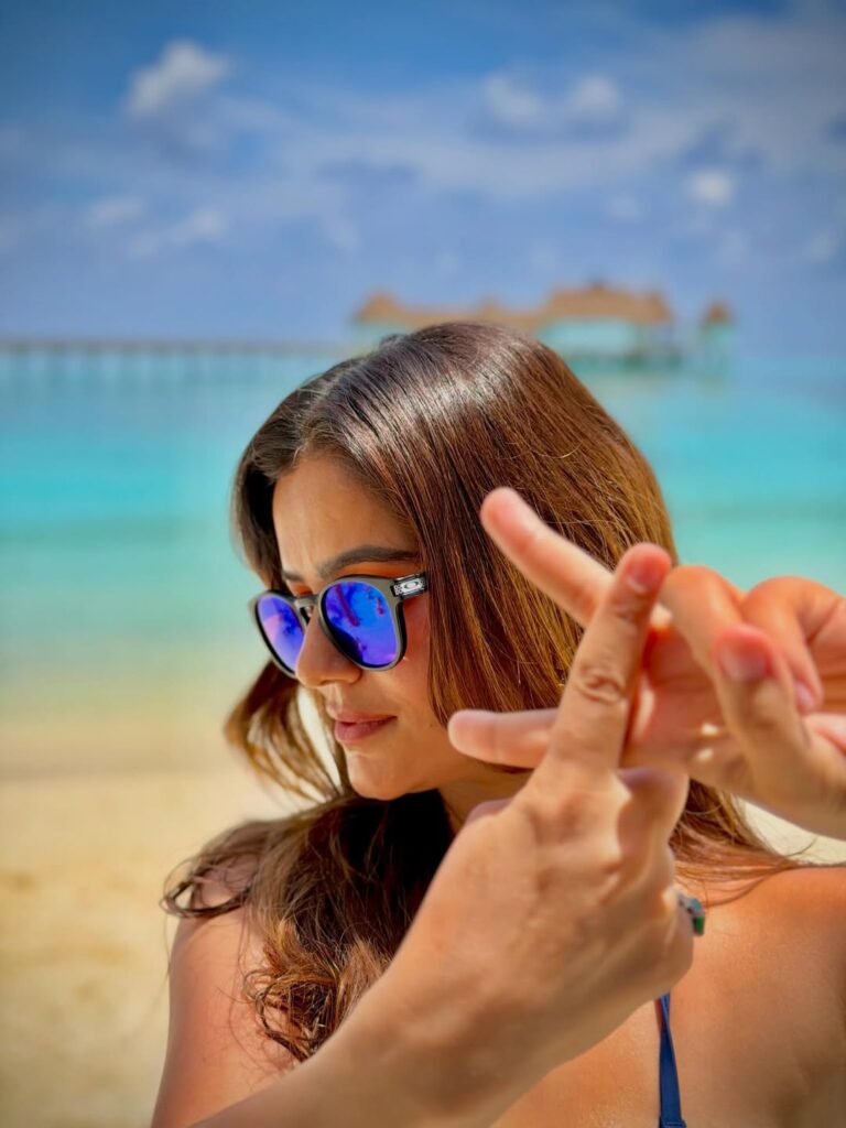 Female contestant of Khatron Ke Khiladi 15 taking a selfie at the beach with sunglasses.