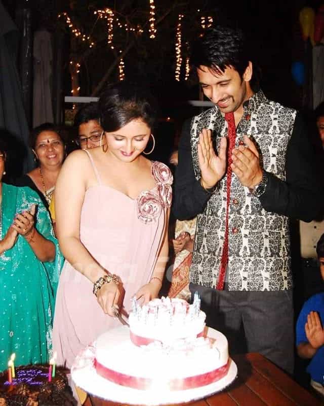 Happy young couple cutting a birthday cake at a festive gathering.
