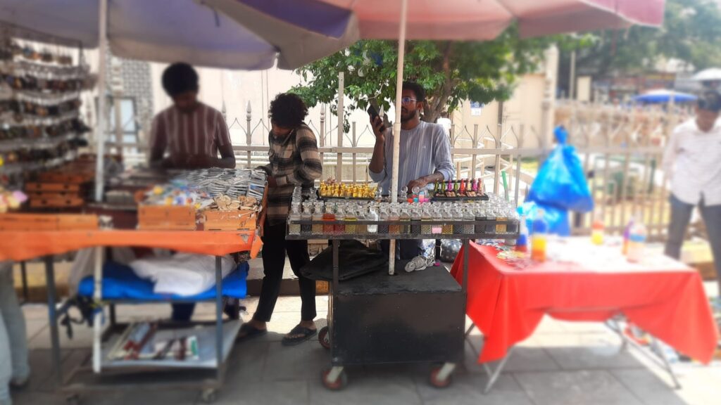 Bright outdoor market stall selling colourful jewelry and accessories under umbrellas in a busy street sc.