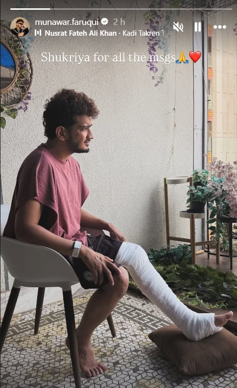 Young man with a leg cast sitting on a chair, holding his injured leg, in a cozy indoor setting with plan.