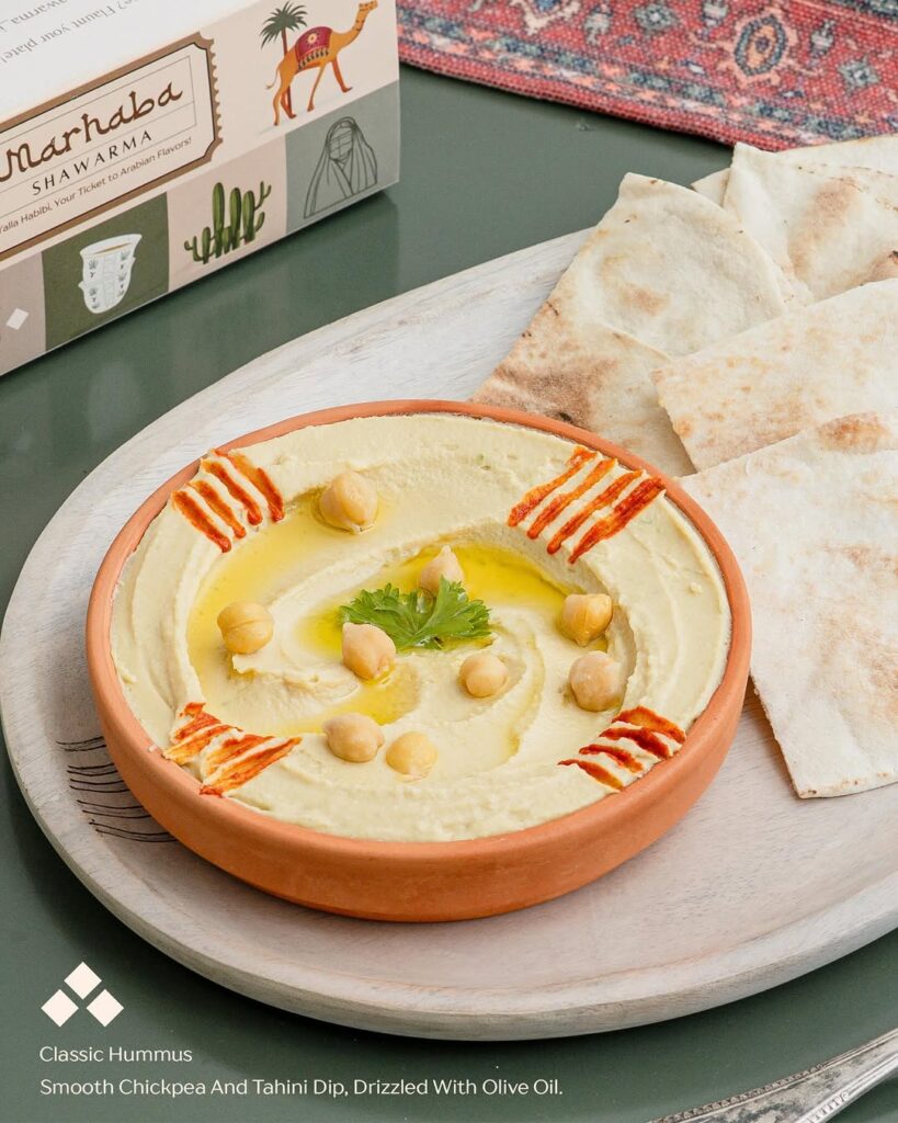 Creamy hummus with chickpeas, tahini dip, garnished with olive oil, cilantro, and paprika, served with fl.